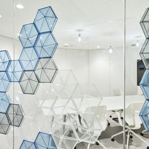 Cluster of hexagonal-shaped transparent and semi-transparent panels with small perforations, arranged in a geometric pattern on a glass wall, showcasing a modern and minimalist aesthetic